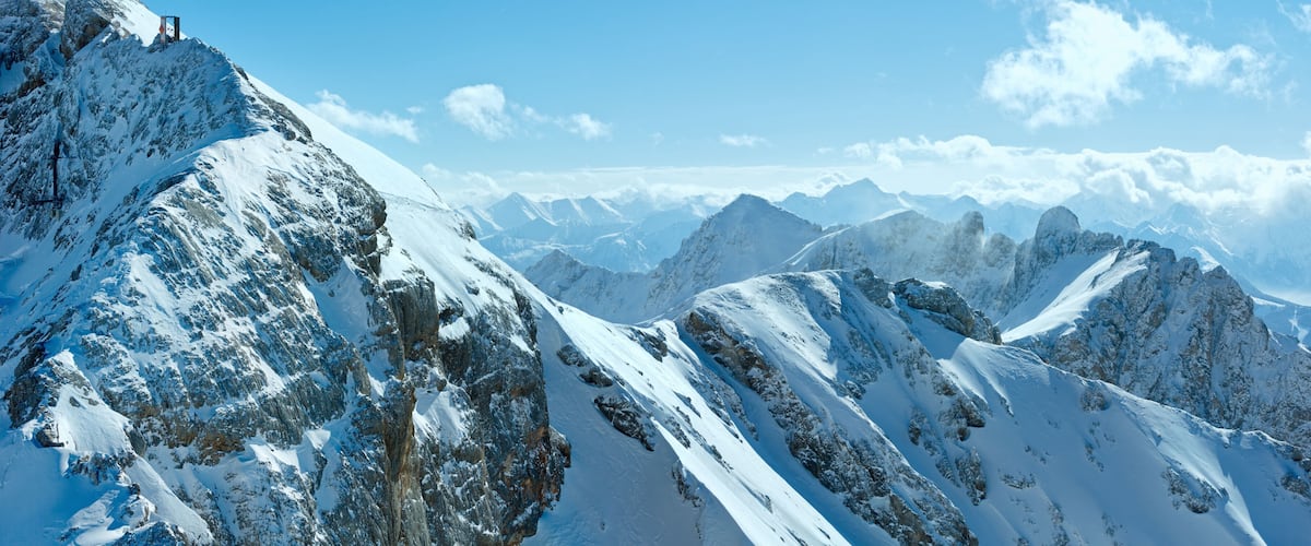 A snow-covered mountain range with rocky outcrops and a clear blue sky.