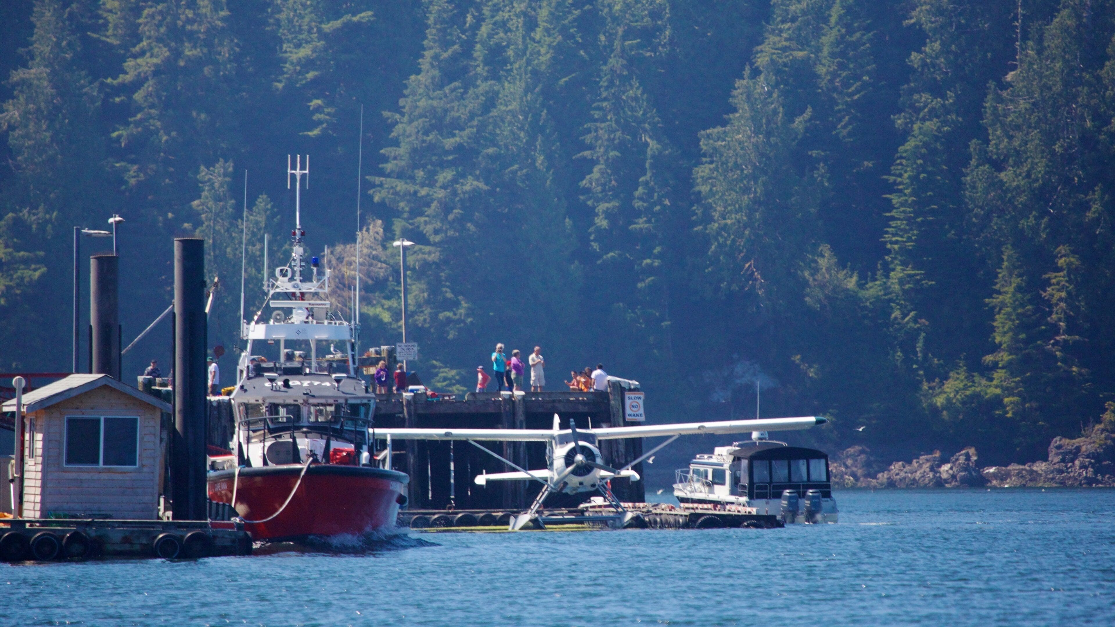 A red boat docked at a pier with a seaplane on a trailer.