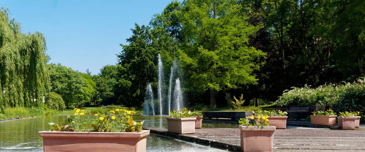 A serene park with a fountain, lush greenery, and flower planters.