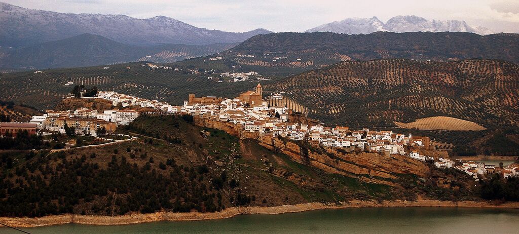 A town nestled in a valley with a prominent church, surrounded by mountains and a lake.
