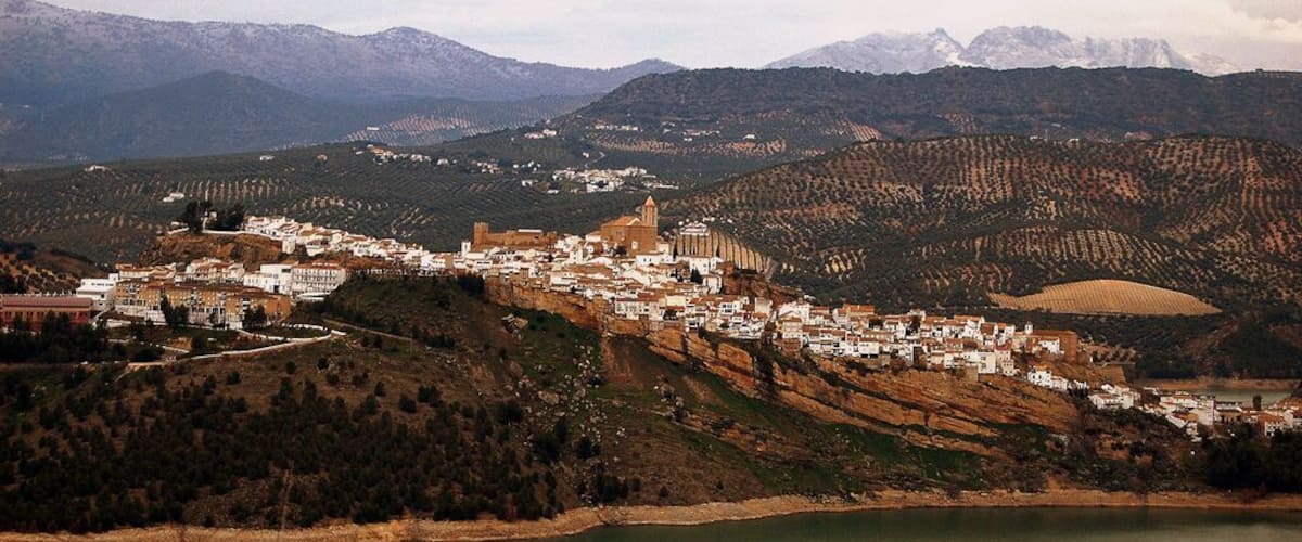 A town nestled in a valley with a prominent church, surrounded by mountains and a lake.