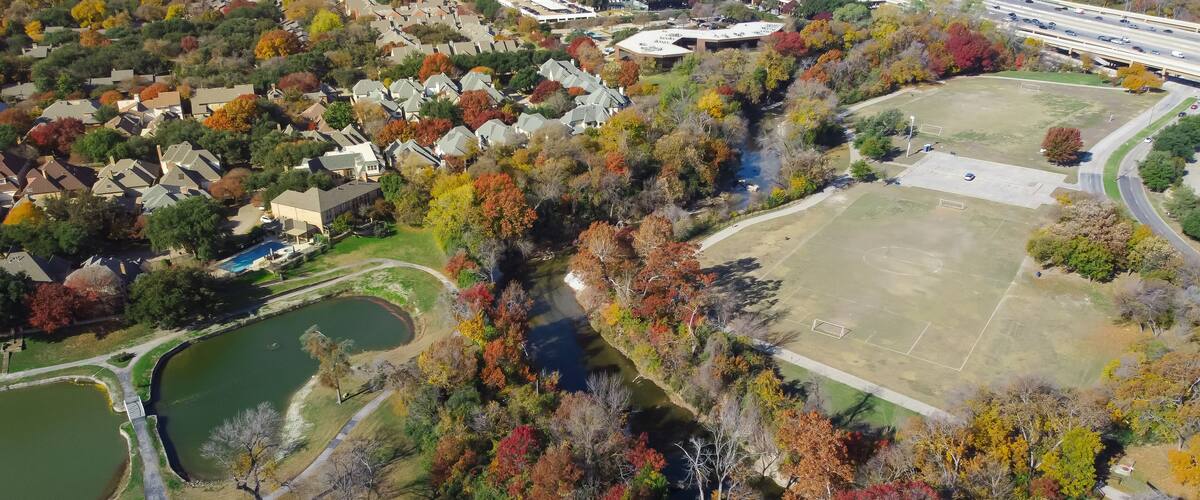 Colorful fall foliage at Park Central with luxury lakeside residential houses, soccer fields, White Rock Creek near major highways North Dallas, Texas, affluent neighborhood community aerial