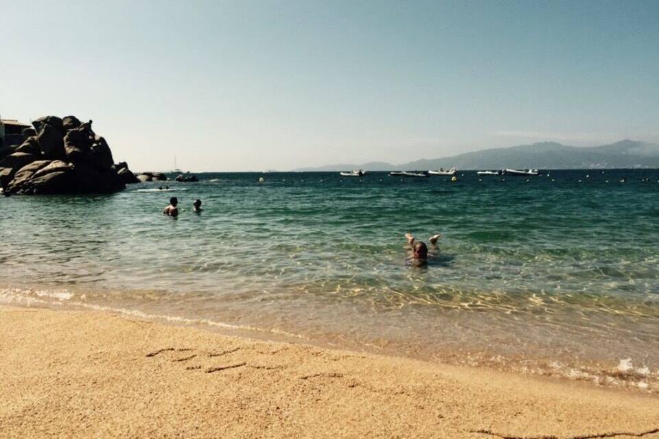A beach with clear water, people swimming, and boats in the distance.