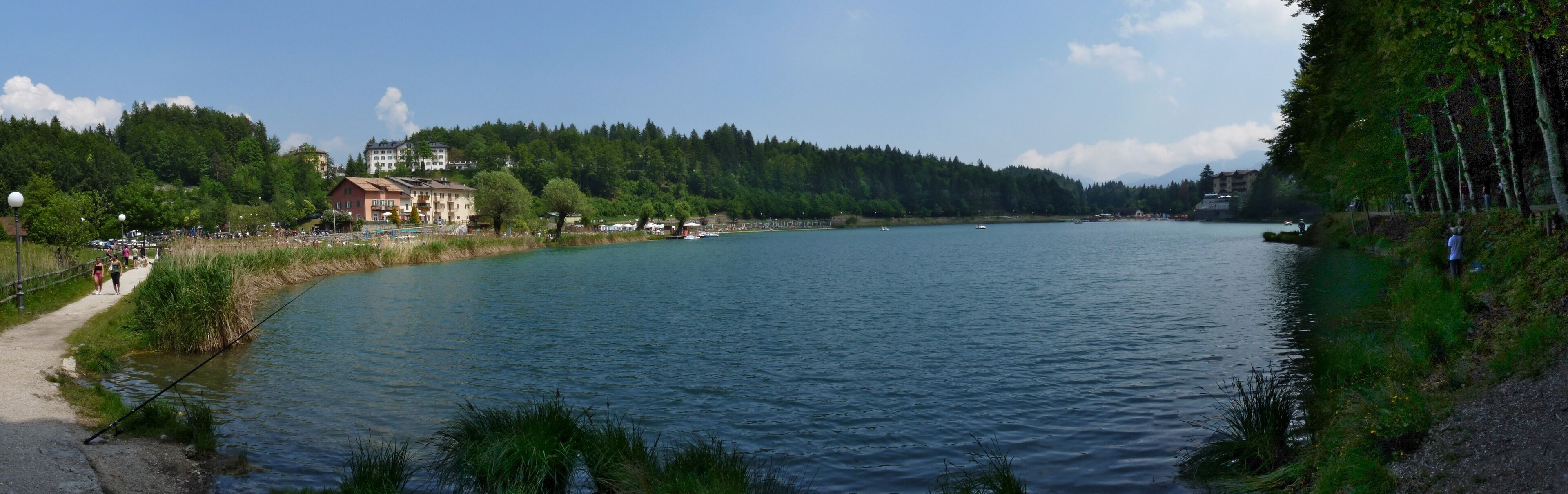 A calm river with a path on the left, surrounded by trees and buildings.