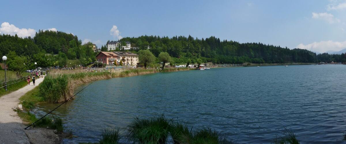 A calm river with a path on the left, surrounded by trees and buildings.