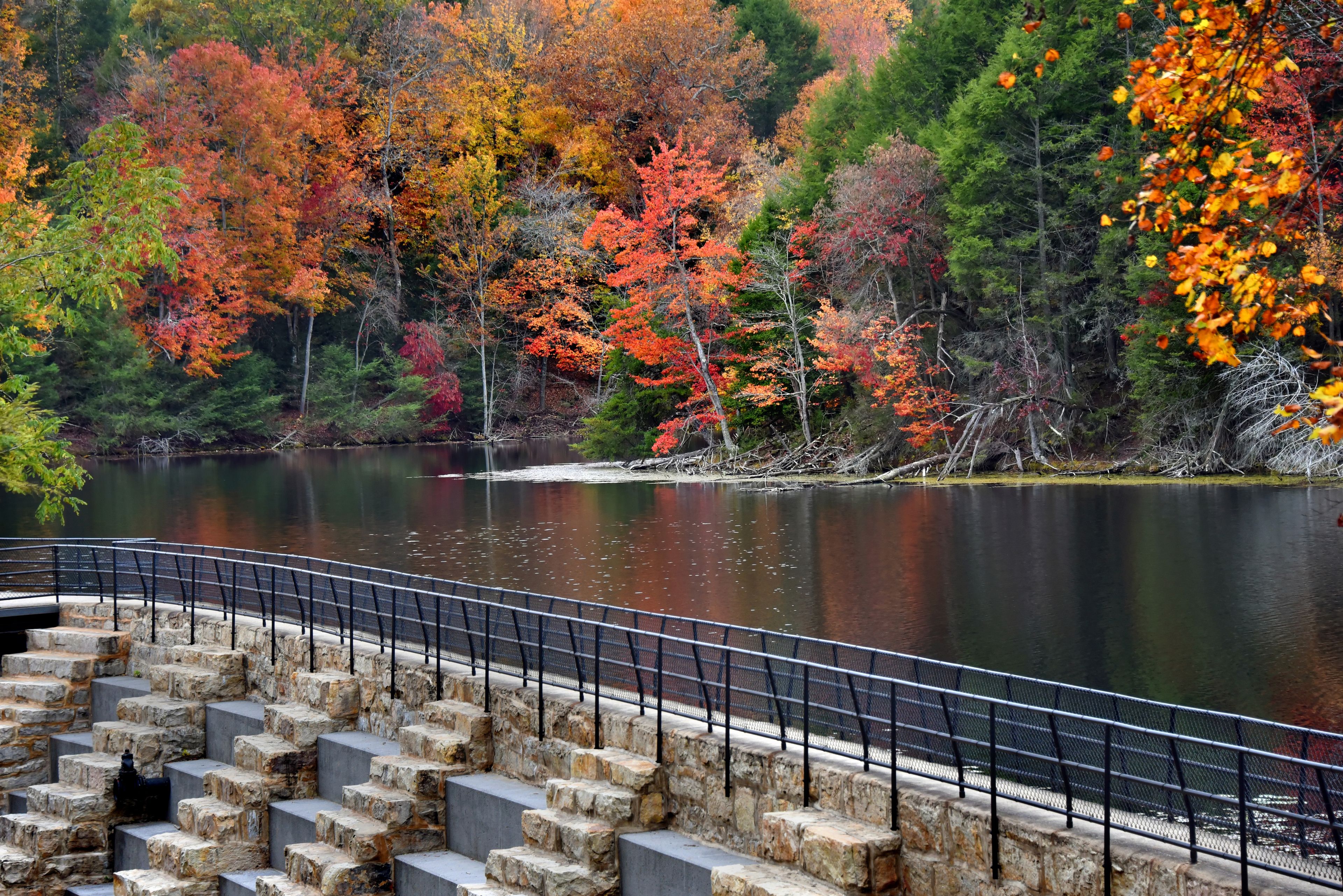 A stone staircase leading to a bridge over a calm lake surrounded by autumn-colored trees.