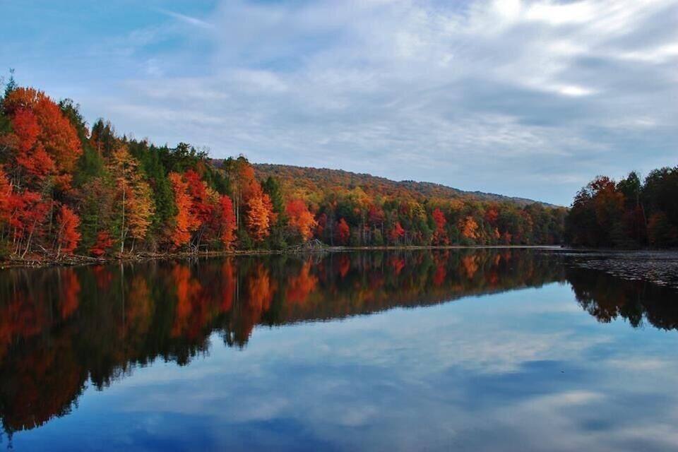 A calm lake reflecting autumn trees with red, orange, and green foliage.