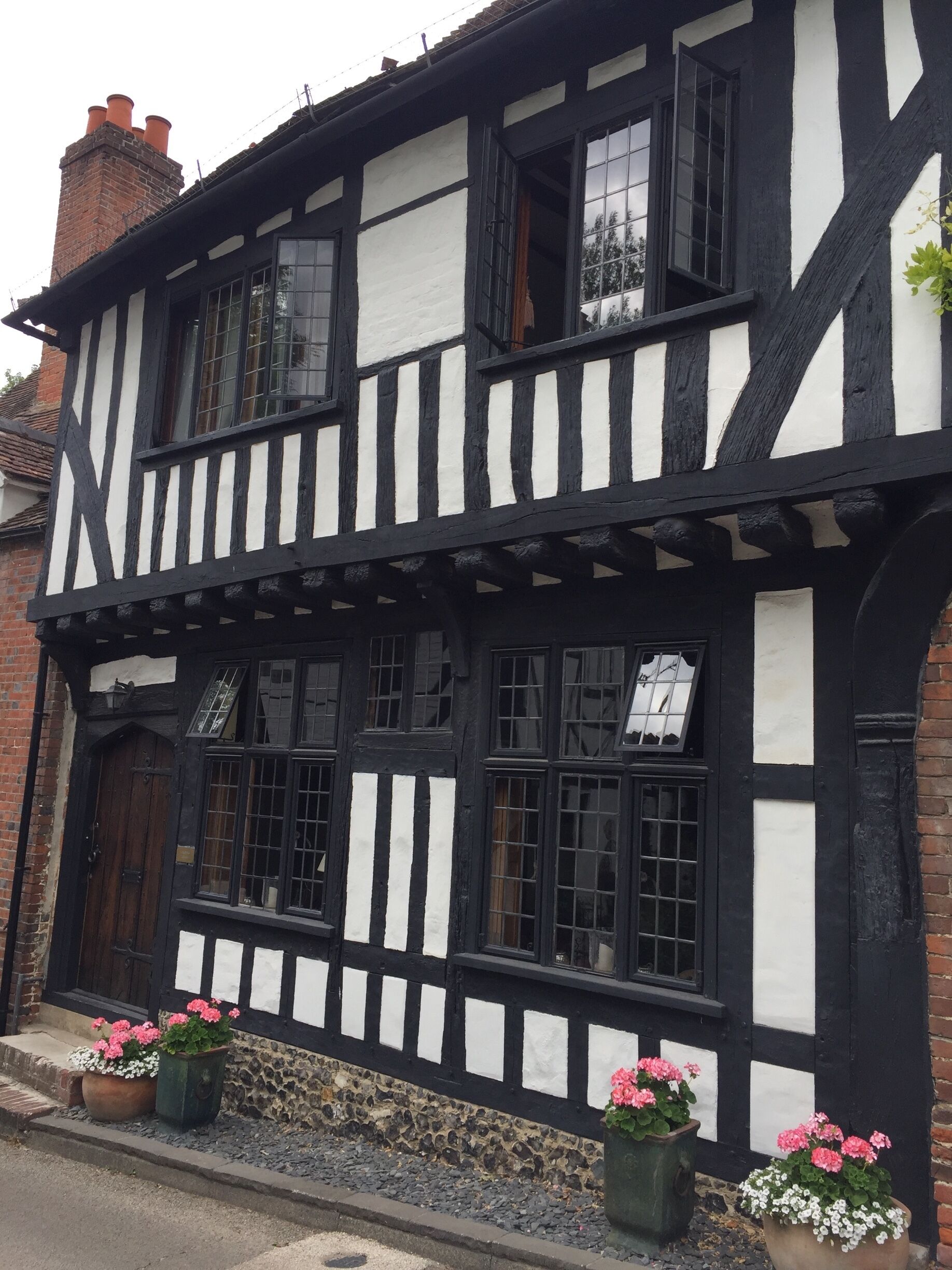 A Tudor-style building with black and white timber framing, large windows, and flower pots on the ground.