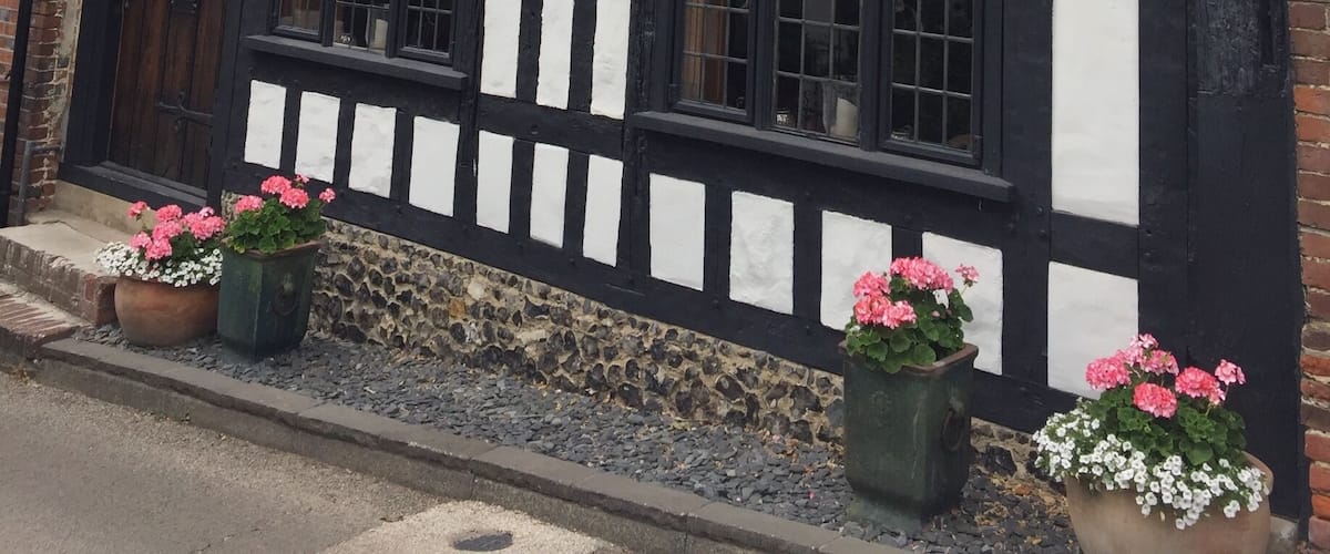 A Tudor-style building with black and white timber framing, large windows, and flower pots on the ground.