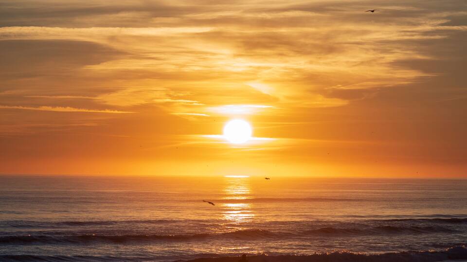 A sunset over a beach with waves and a person cycling.