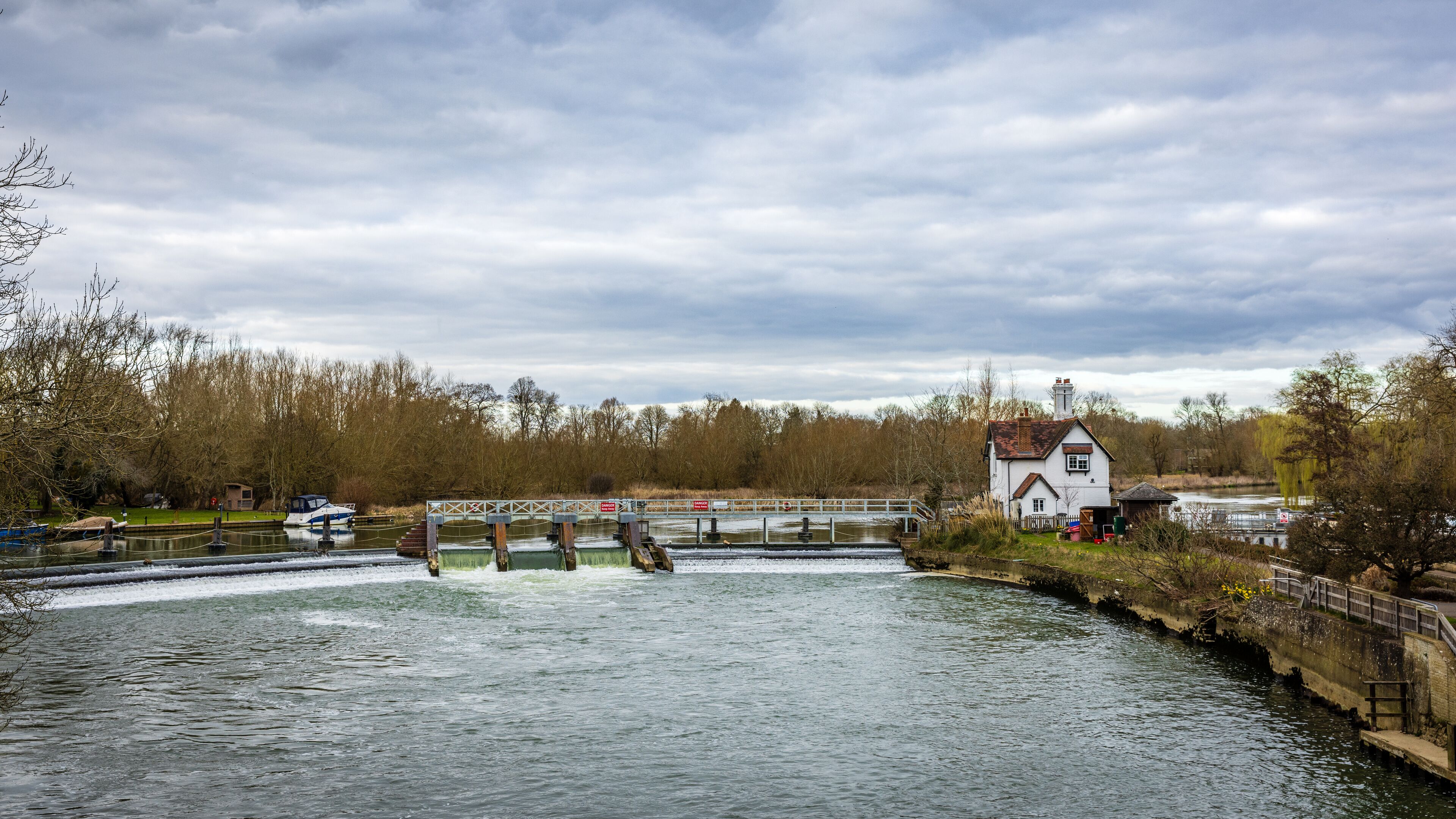 A river with a lock system, a white house, and trees in the background.