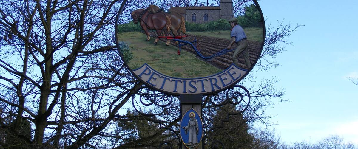 A signpost with a coat of arms and a depiction of a horse-drawn plow, indicating a historical or agricultural significance.