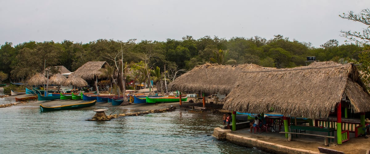 A riverside village with thatched-roof huts and colorful boats.