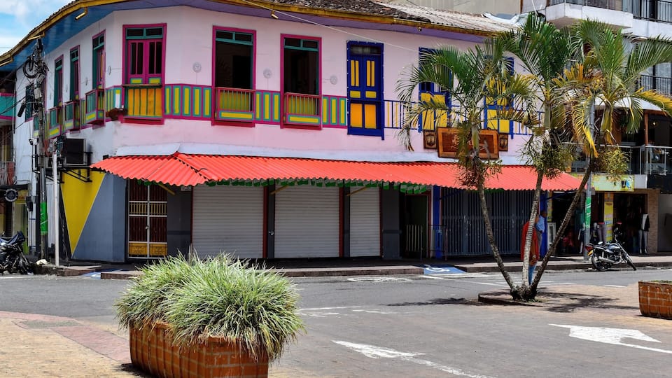 A colorful building with a red awning, a palm tree, and a parked motorcycle.
