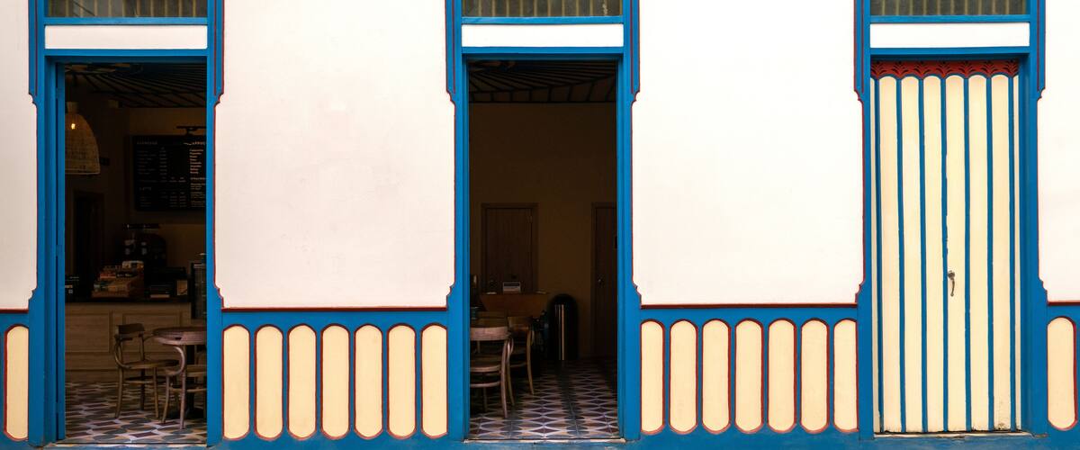 A building with blue-framed doors and windows, a tiled floor, and a visible interior with tables and chairs.