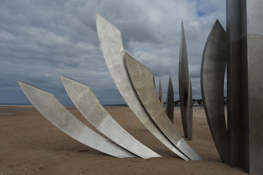 A series of metallic sculptures on a sandy beach with a cloudy sky.
