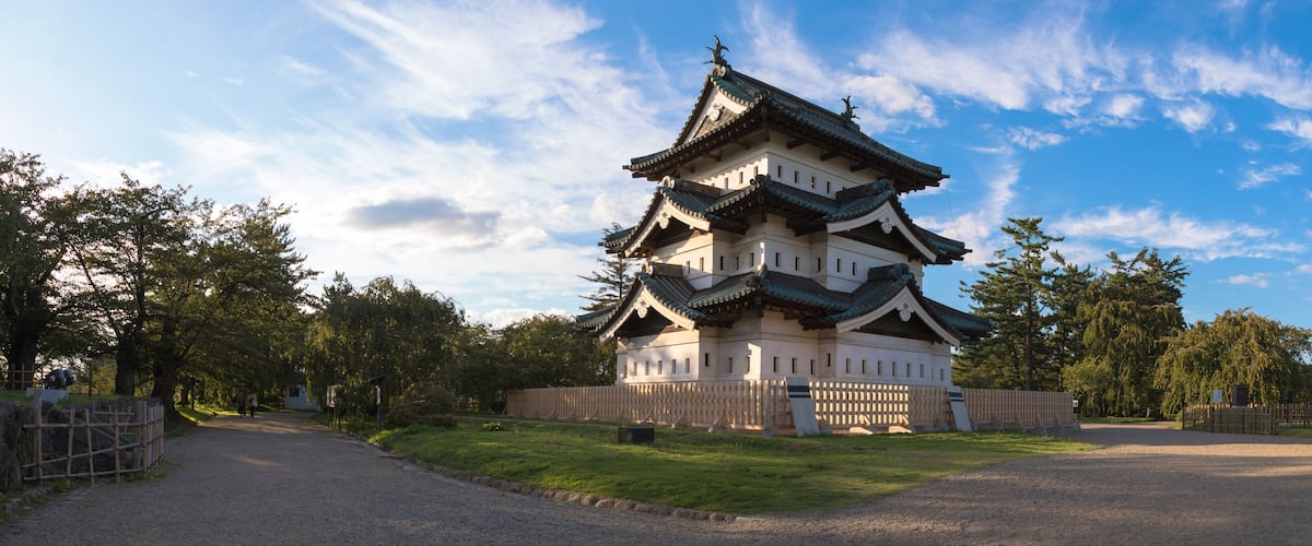 A traditional Japanese pagoda with multiple tiers and a green roof, surrounded by a wooden fence and trees.