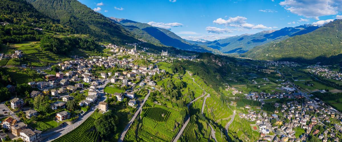 A valley with a town nestled among mountains, vineyards, and a prominent church tower.