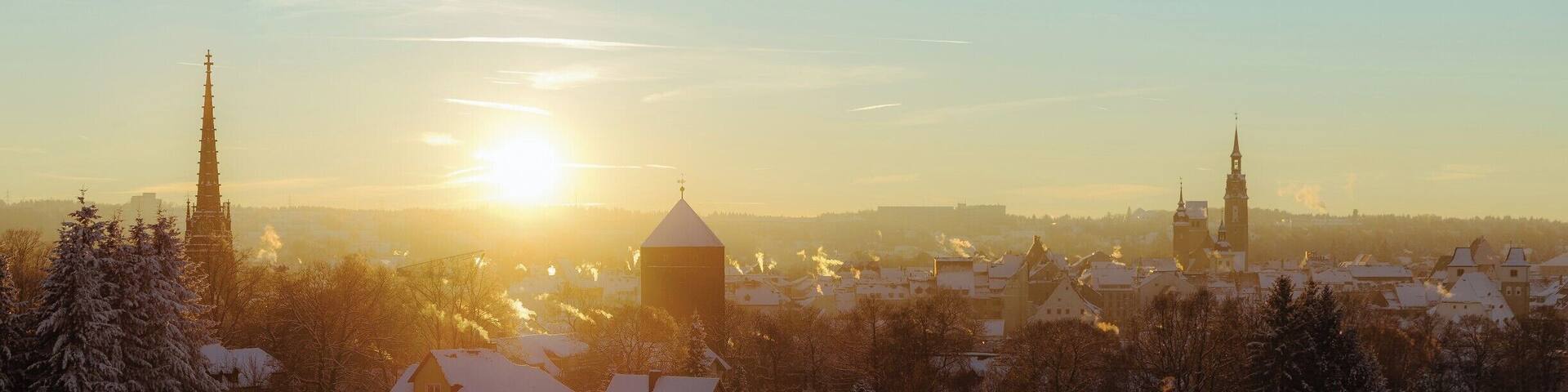 A snow-covered village with a prominent church tower and a large building with a dome, under a setting sun.