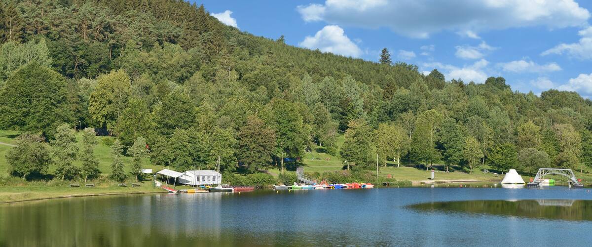 A lake with boats, a white house, and a forested hill.