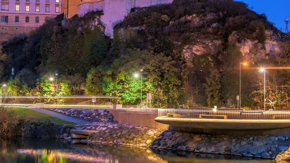 A cathedral with twin towers, a river reflecting its structure, and surrounding greenery.