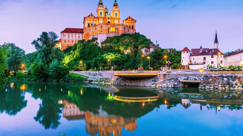 A historic church with twin towers and a reflection in a calm body of water.