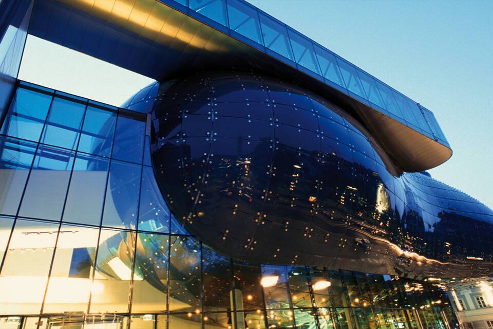 A modern glass building with a curved facade reflecting city lights.