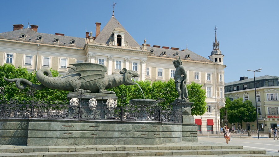 Una estatua de un dragón y un hombre en una plaza con una fuente, frente a un edificio histórico.