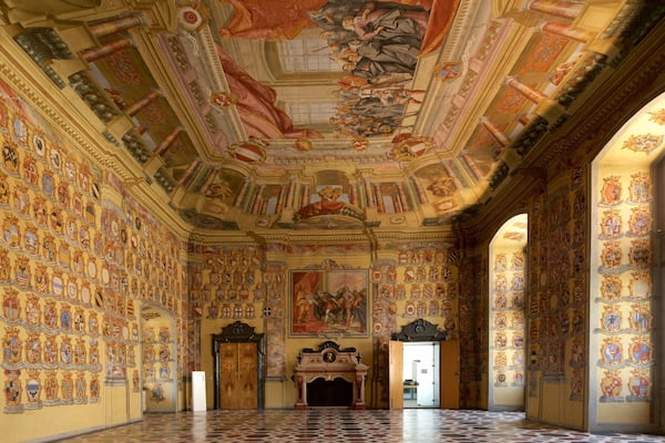 Un vaste hall doté de plafonds richement décorés, d’une grande fresque murale et de nombreuses armoiries sur les murs.