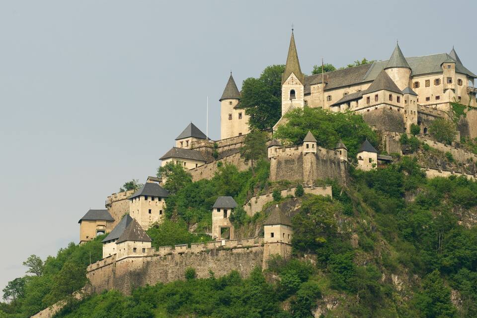 Eine historische Burg thront auf einem Hügel, umgeben von üppiger Vegetation.
