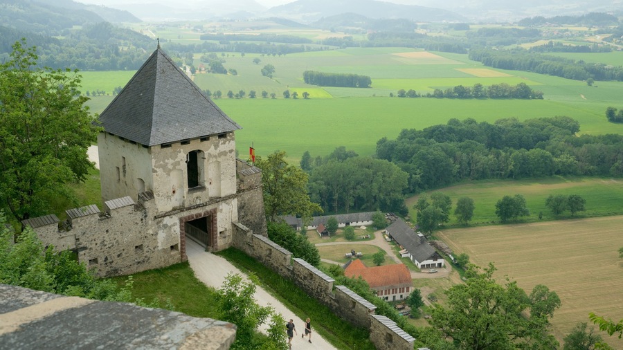 A historic stone castle with a conical roof overlooking a lush green valley.
