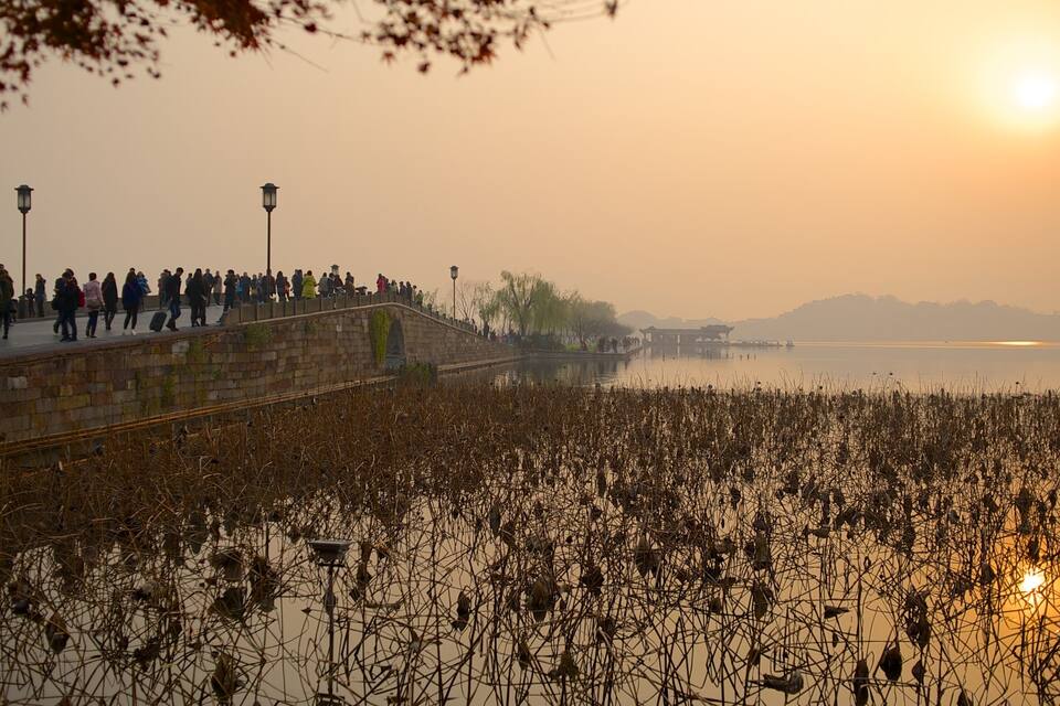 A sunset over a body of water with a stone bridge and people walking on it.