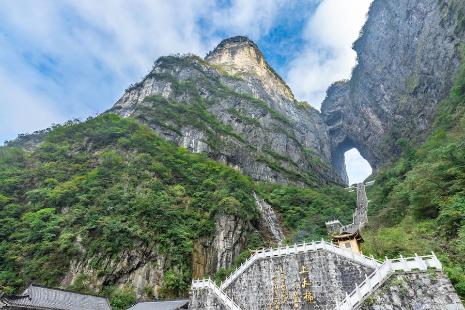 A mountainous landscape with a temple and a large rock arch formation.