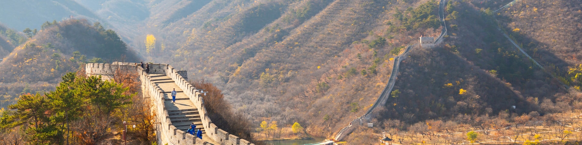 The Great Wall of China winding through a mountainous landscape with a river and traditional Chinese architecture.