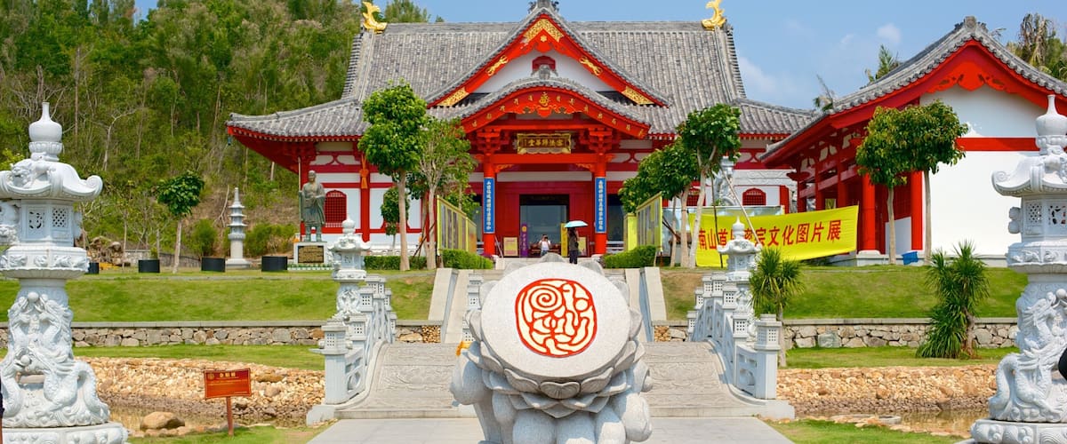 A traditional Chinese temple with red and white architecture, surrounded by stone lanterns and a central stone sculpture.