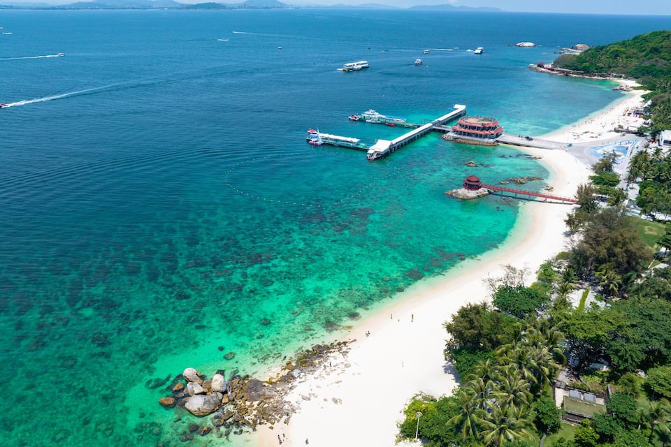 A coastal area with clear turquoise waters, a sandy beach, and a pier extending into the sea.