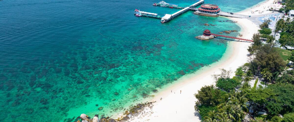 A coastal area with clear turquoise waters, a sandy beach, and a pier extending into the sea.