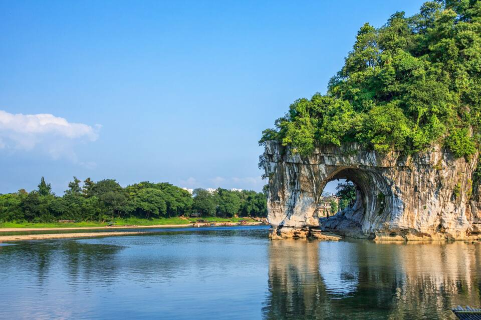 Un río con una formación natural de arco de roca rodeado de vegetación exuberante.