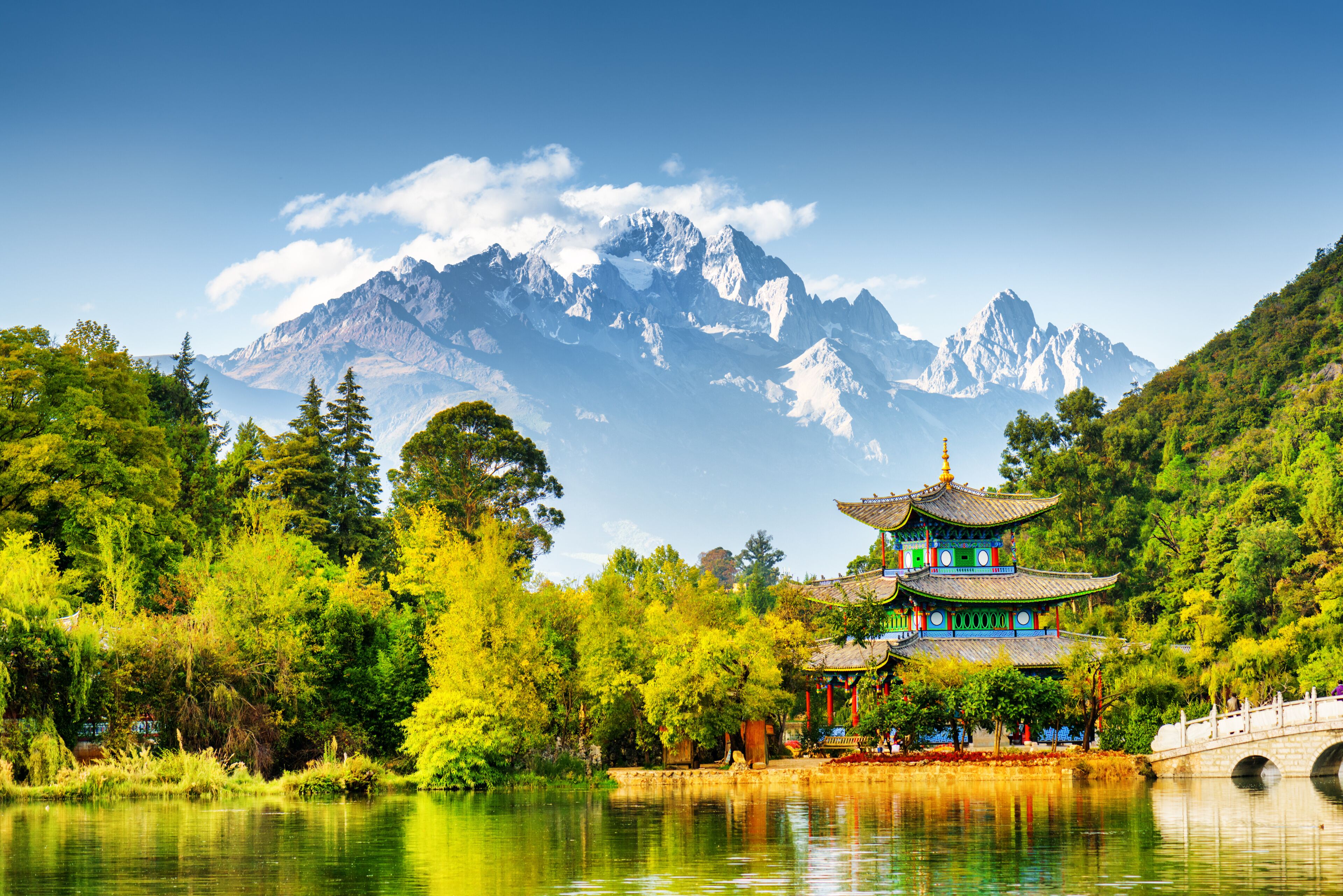 A traditional pagoda by a lake with mountains in the background.