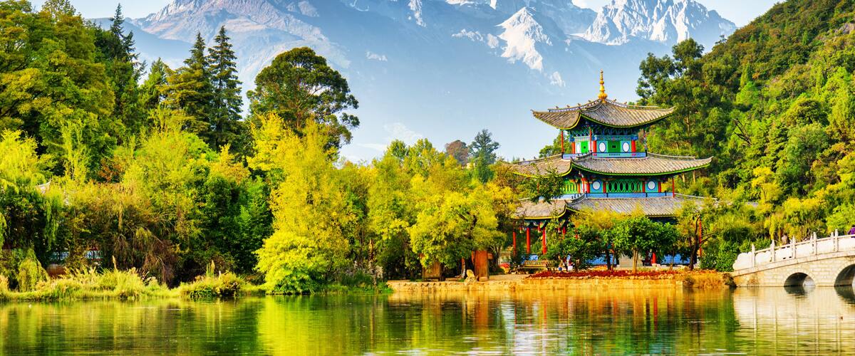 A traditional pagoda by a lake with mountains in the background.