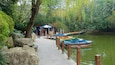 Une promenade le long de la rivière, avec des bateaux aux couleurs vives amarrés sur la droite, le tout entouré d’une végétation luxuriante et d’arbres.