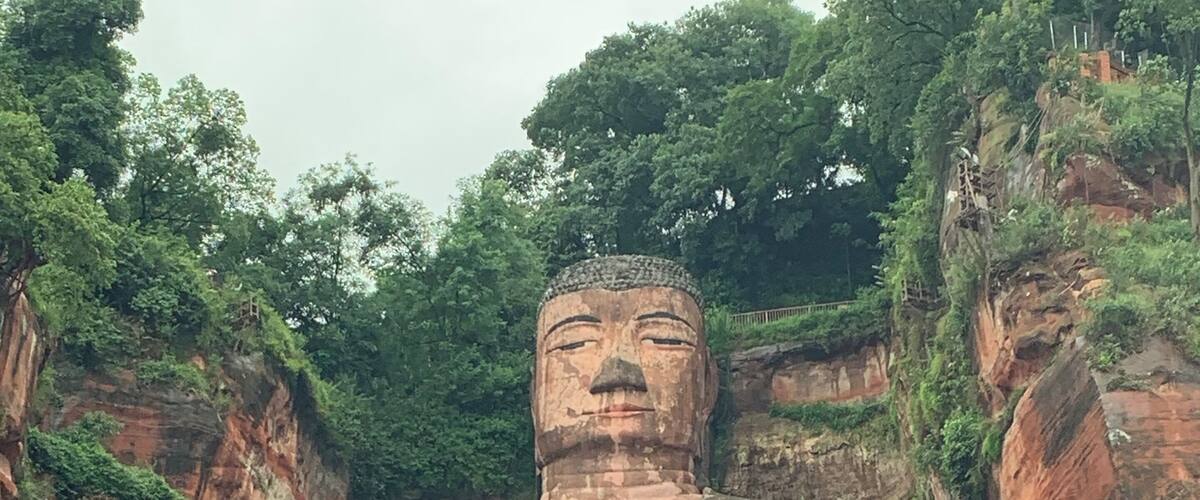 A large Buddha statue carved into a cliff face, surrounded by lush greenery.