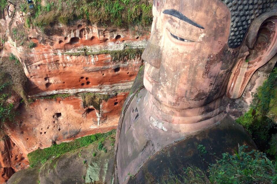 A large Buddha statue with a cliff face in the background.