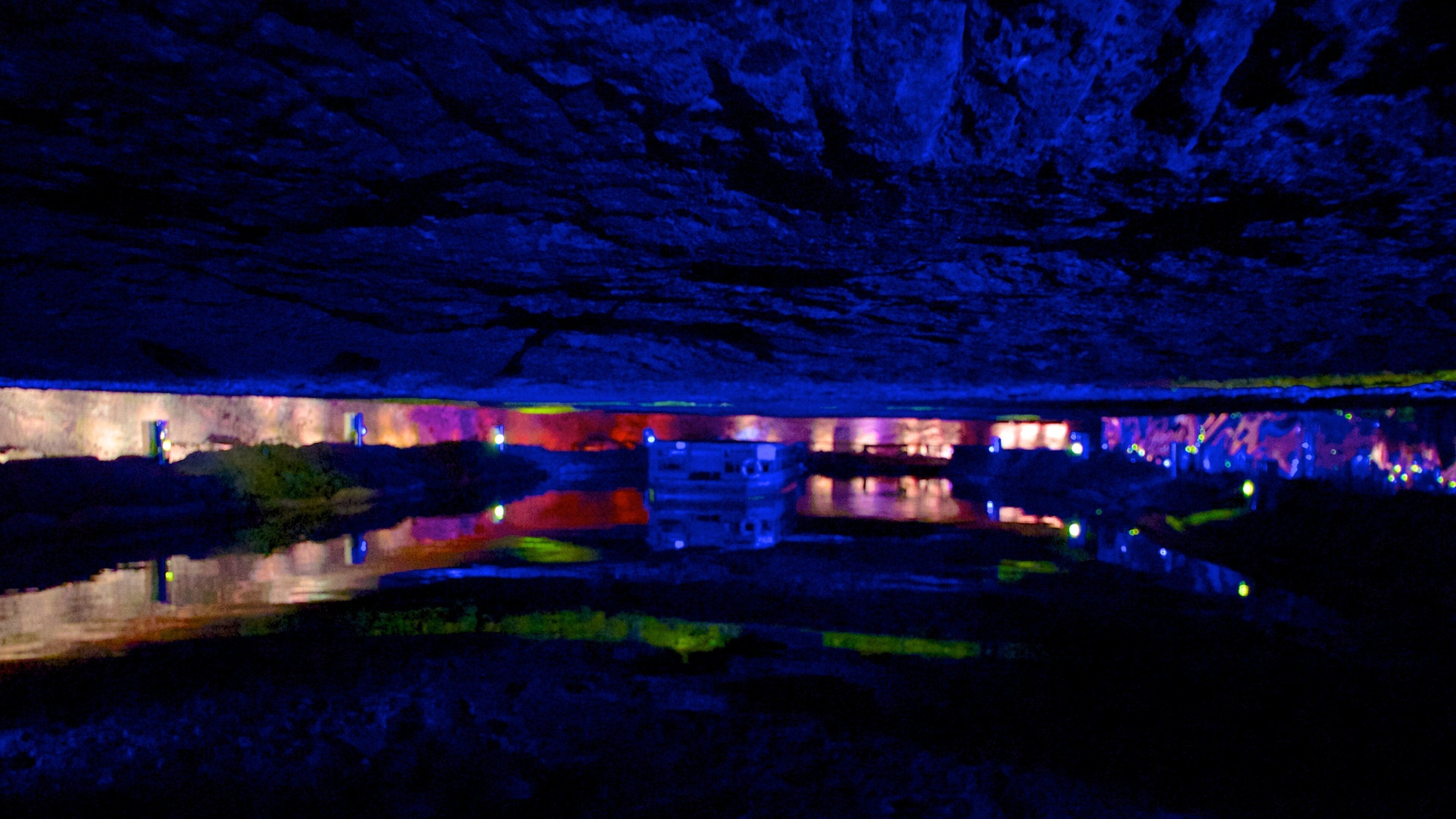 A cave illuminated with colorful lights reflecting on a water surface.