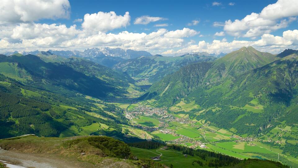 A mountainous landscape with a valley, a small town, and snow-capped peaks in the distance.