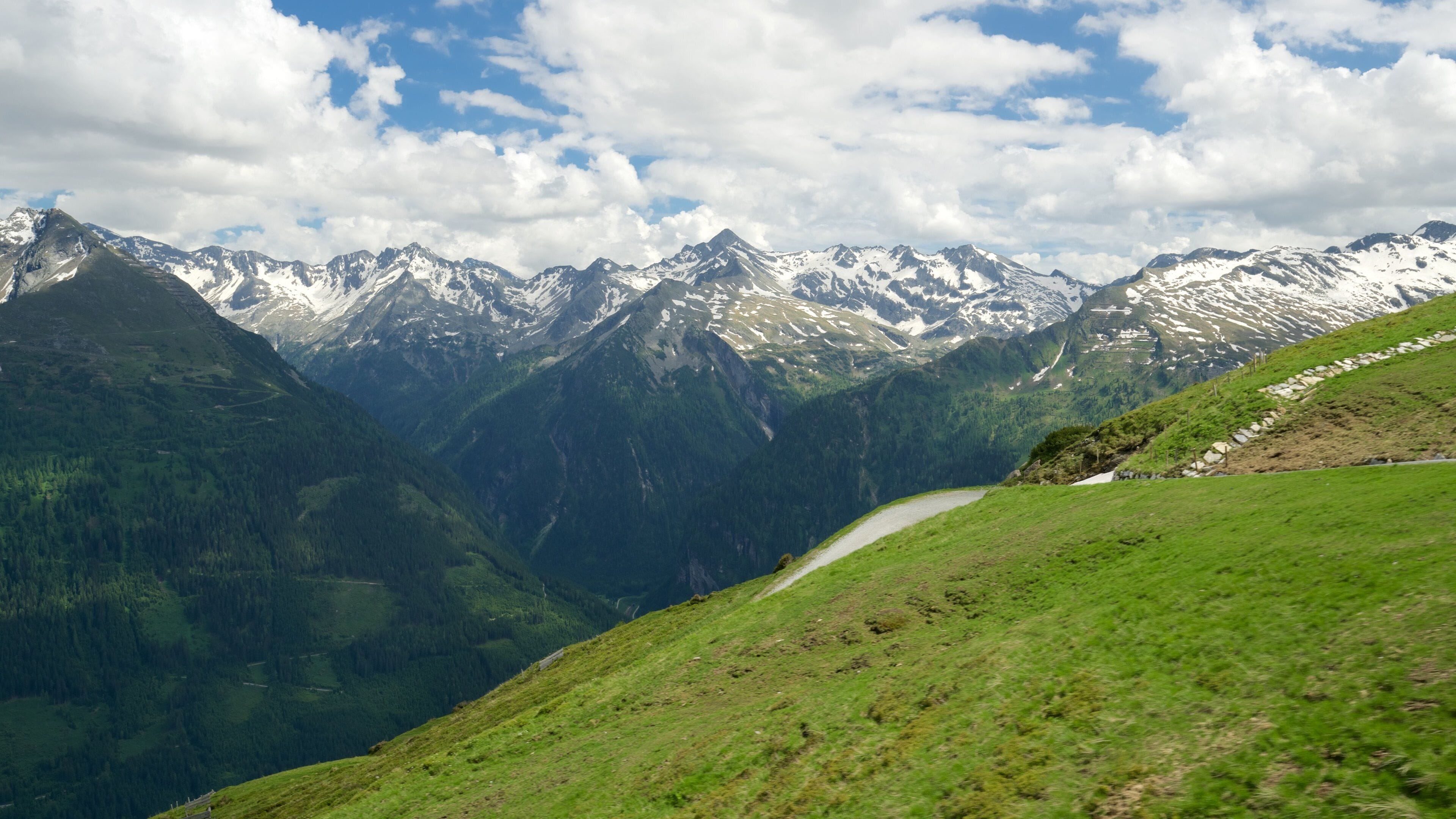 A mountain landscape with a winding road, snow-capped peaks, and lush green valleys.