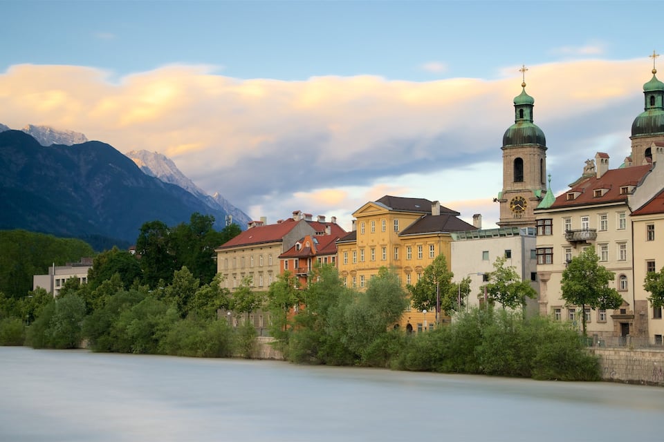 A historic town with colorful buildings, a river, and mountains in the background.