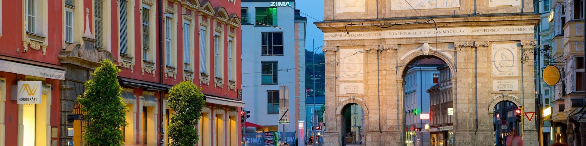 A historic city square with a prominent archway, tram tracks, and classic European architecture.