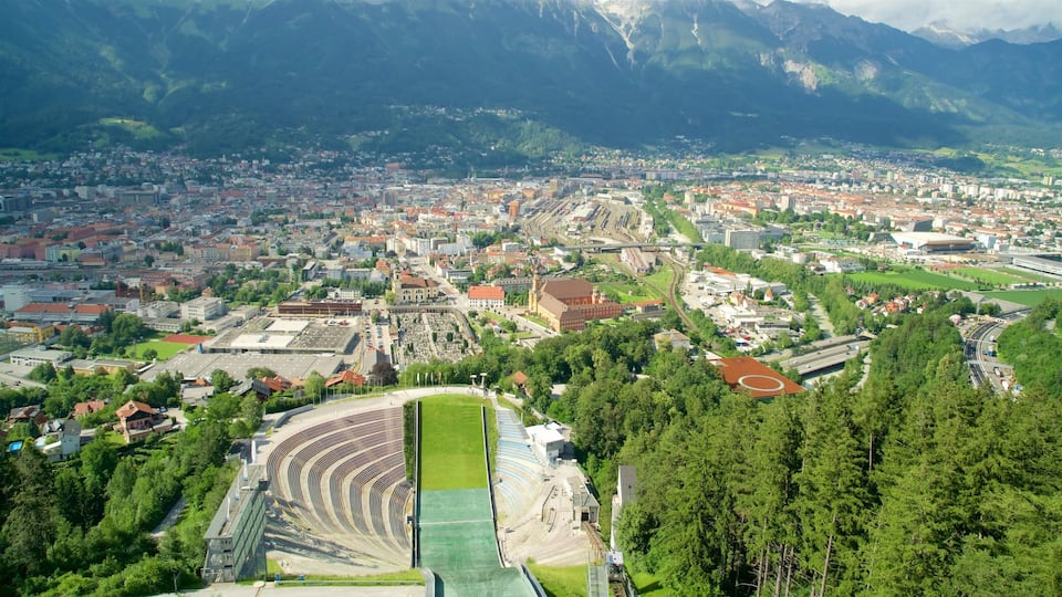 An aerial view of a city with a large stadium, surrounded by mountains and greenery.