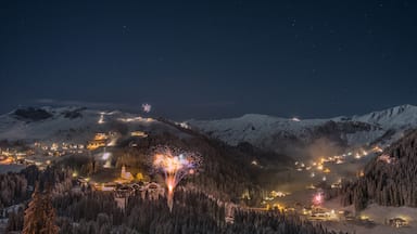Cordillera nevada en la noche con un pueblo abajo y fuegos artificiales al frente.